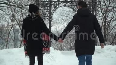 年轻的男人和女人在冬天的公园里散步，白雪覆盖着双手。 冬闲的幸福恩爱夫妻.. 回去